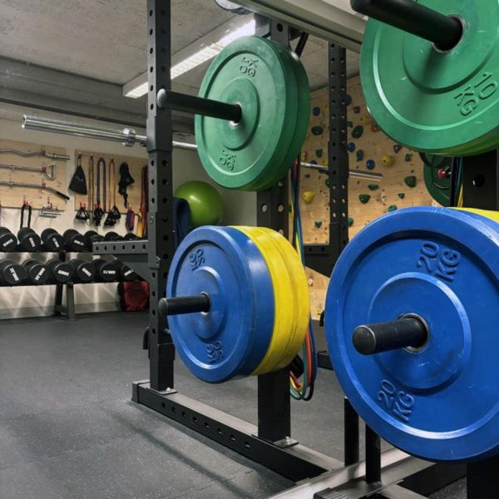 Intérieur de salle de sport avec des racks, des poids, des haltères et un mur d'escalade.